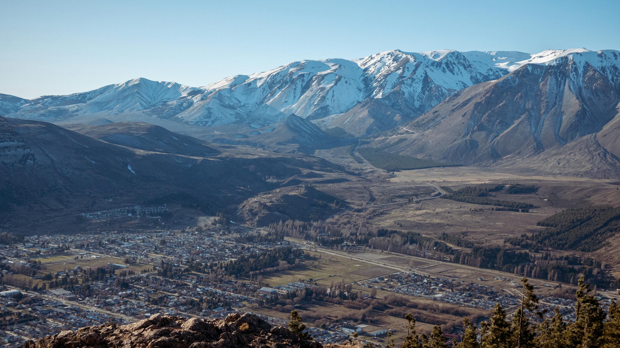 Breathtaking aerial view of a town against snow-capped mountain backdrop under clear blue sky.